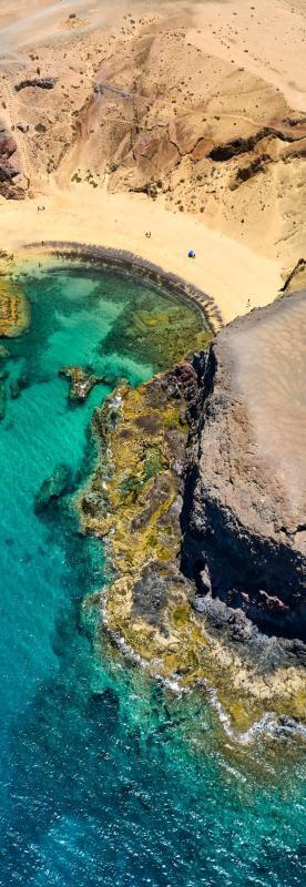 Vista aérea da praia do Papagayo em Lanzarote, com areia dourada, falésias vulcânicas e mar turquesa.
