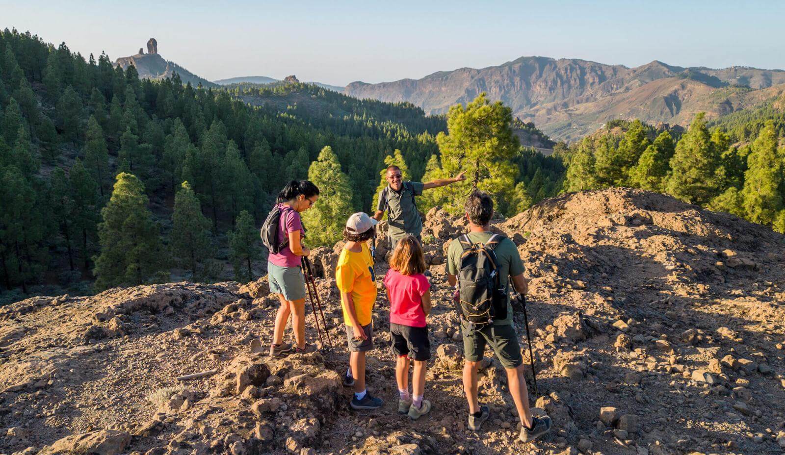 Excursão em grupo pelo Parque Rural do Roque Nublo, entre solo rochoso, pinhal canário e o pico ao fundo.