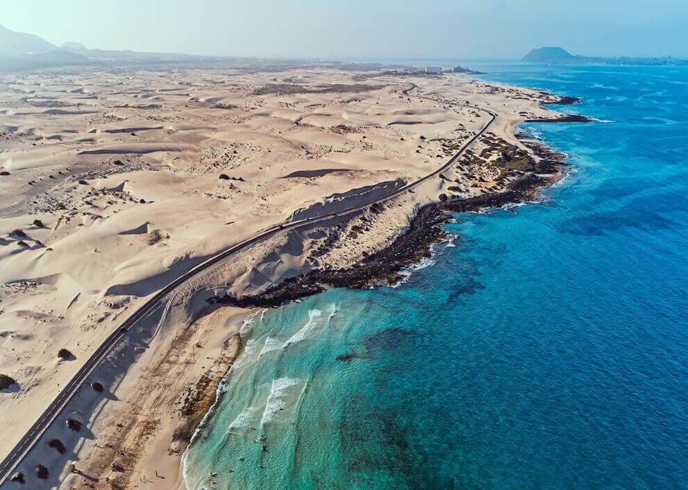 Vista aérea das Dunas de Corralejo em Fuerteventura, com extensos areais à beira de um mar turquesa.